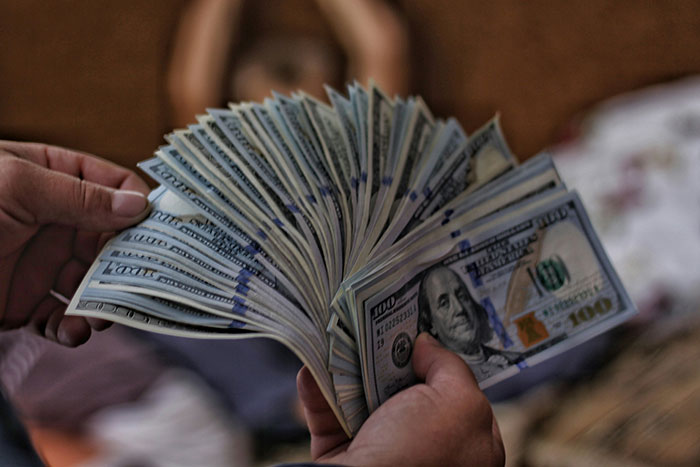 Hands holding a fanned out stack of hundred-dollar bills, illustrating frugality concerns.