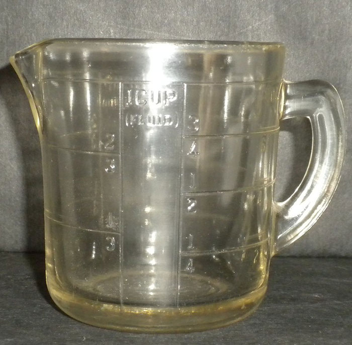 Clear plastic measuring cup illustrating frugality with regrets due to its worn appearance.