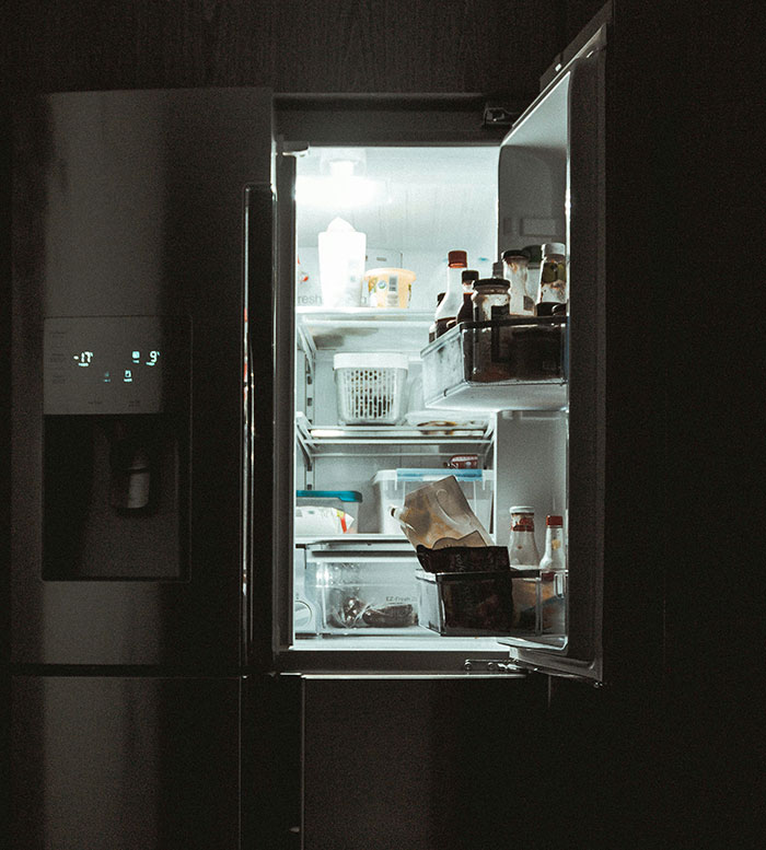 Open fridge with assorted items, illustrating frugality in a dimly lit kitchen.