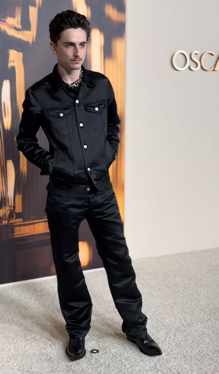 Man in black outfit at Oscar nominees dinner, showcasing unique fashion choices.