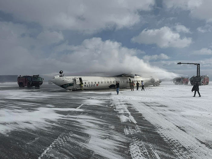 Emergency landing response with plane on snowy runway; firefighters and vehicles present.