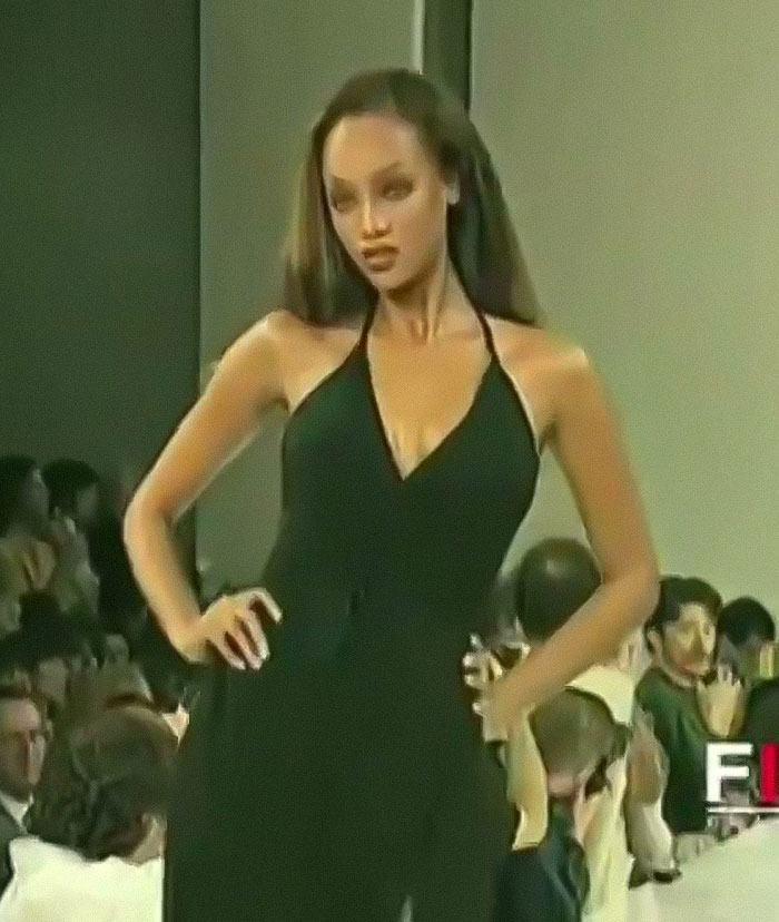 A model in a black dress walking down the runway, capturing attention with her confident expression.