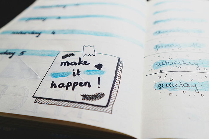 Notebook with "make it happen" written, surrounded by doodles, emphasizing wedding planning.