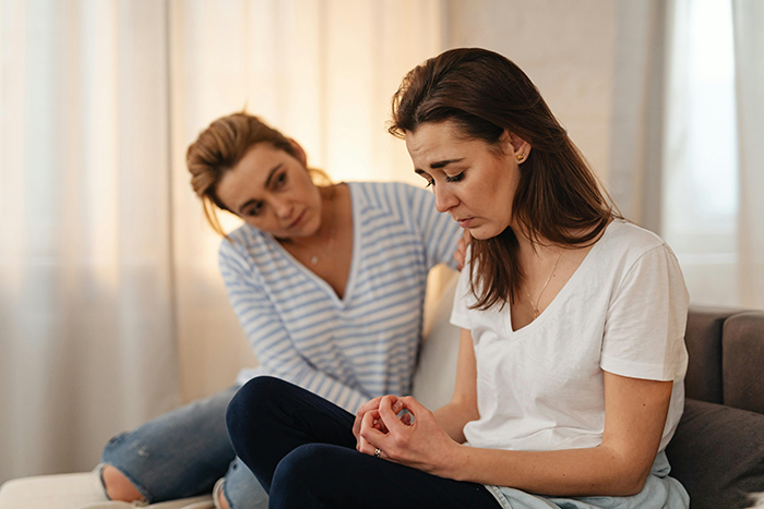 Two women sitting, one consoling the other, discussing a wedding deposit issue.