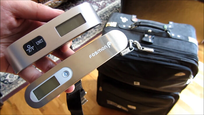 Digital luggage scales next to a suitcase, showcasing travel must-haves for improved packing efficiency.