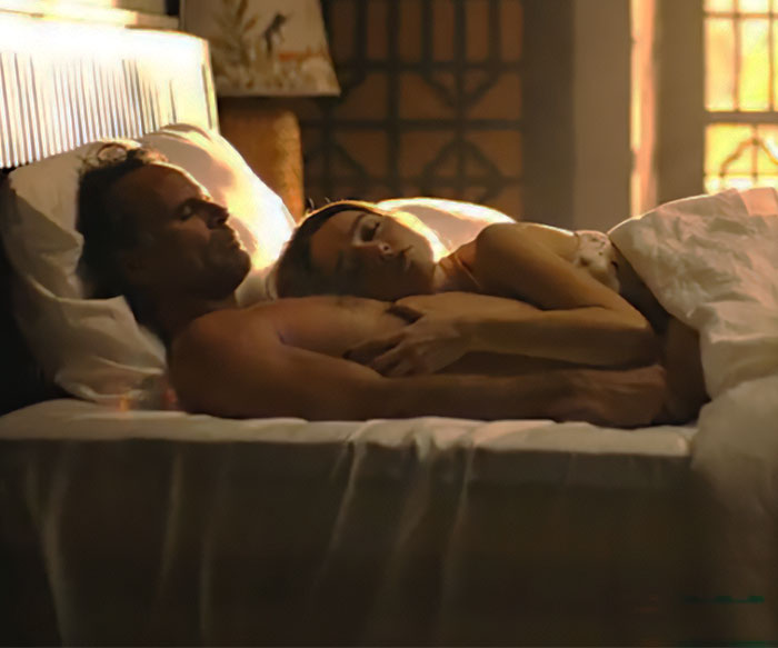 Couple lying in bed during an intimate scene, evoking discussion on intimacy coordinators in film.