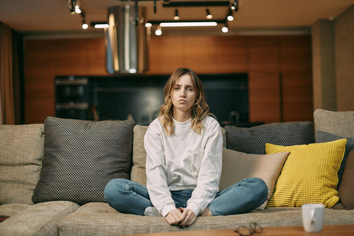 Woman sitting on a couch, looking concerned, highlighting parental financial dependence issues.