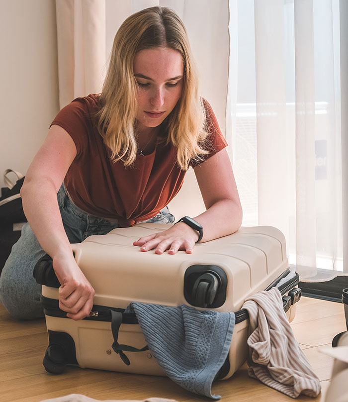 Woman packing suitcase, planning to confront cheating husband, wearing casual clothes in a room with natural light.