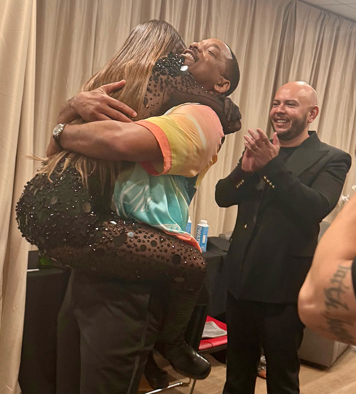 Man embracing a woman backstage as another man watches and claps, creating controversial discussion.