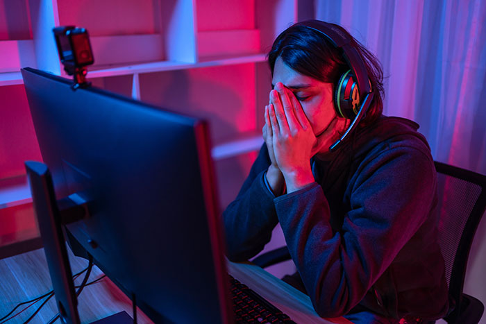 Zoomer M25 disappointed at computer desk in a dimly lit room, wearing headphones.