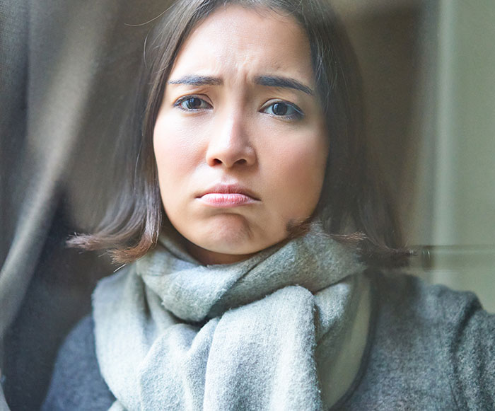 A woman with a sad expression, wrapped in a gray scarf, reflecting on advice after being rejected by her Zoomer friend.