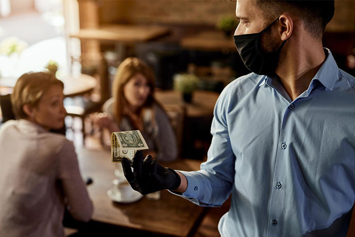 Waiter holding a dollar bill, with two women discussing something in the background at a restaurant.