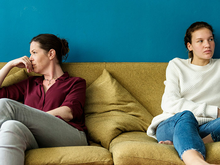 Two women sitting on a couch, looking away from each other, reflecting tension and evidence-seeking.