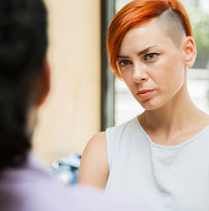 Woman with short red hair looking concerned, wearing a white shirt, represents concept of gender assumptions.