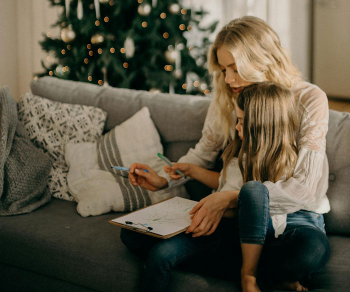 Woman and child sitting on a sofa, surrounded by festive decor, engaging in drawing and coloring activity.