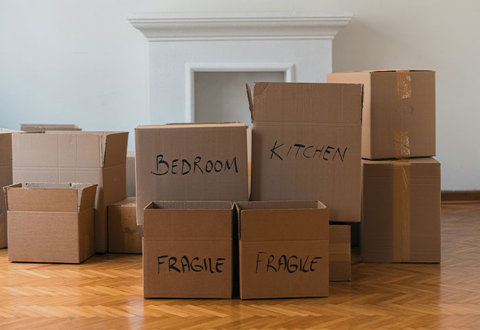 Moving boxes labeled "Bedroom" and "Kitchen" stacked on wooden floor, relating to temporary stay situation.