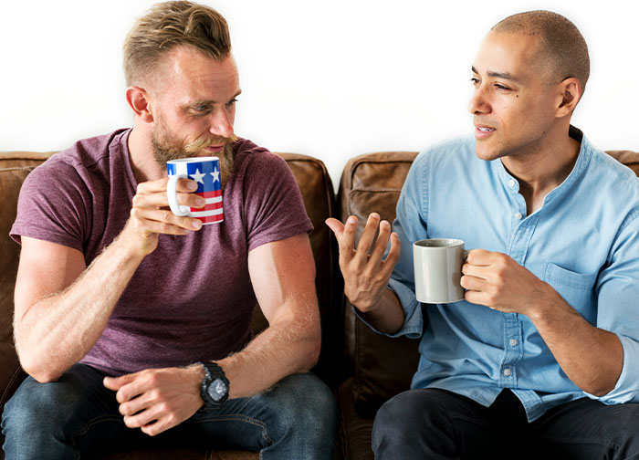 Two friends sitting on a couch, drinking coffee, and discussing the challenge of a prolonged stay.