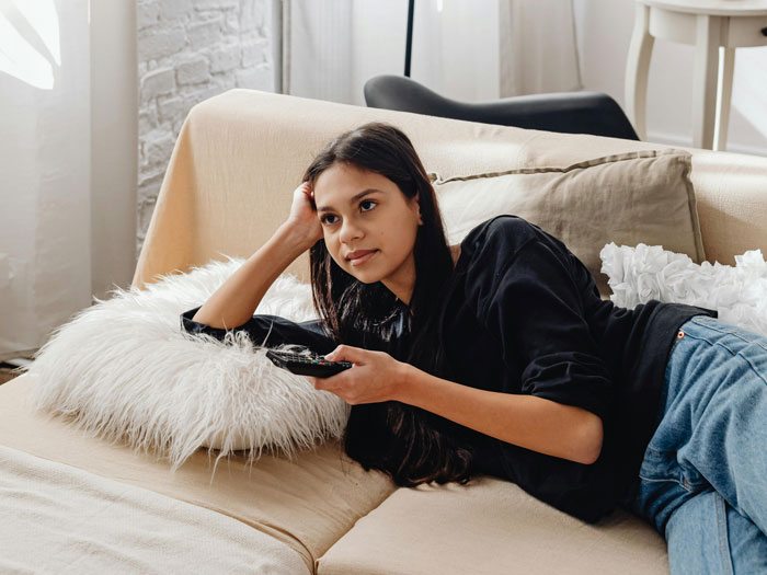 Woman relaxing on sofa with remote, watching TV.