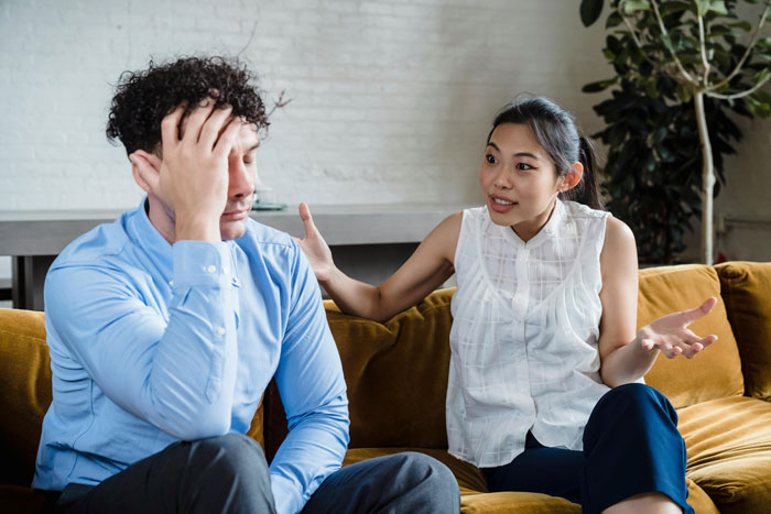 Woman discussing with husband in living room over 'RuPaul’s Drag Race' viewing setup.