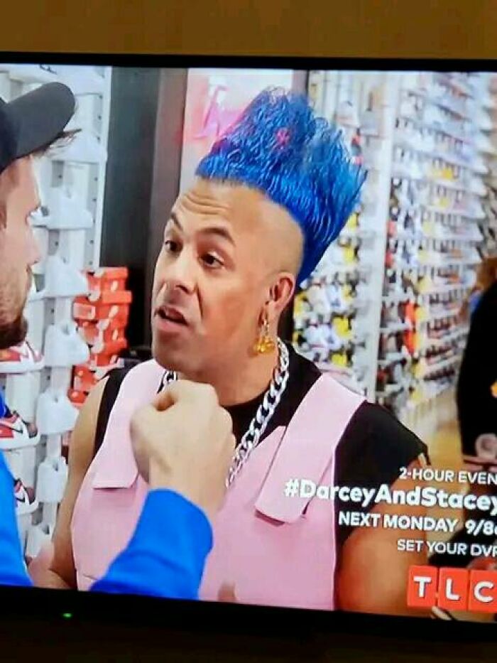 Man with bright blue hairstyle talking to another person in a colorful store setting, showcasing worst hair fails.