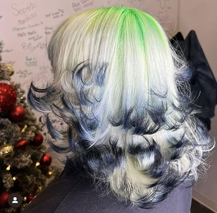 Unique hair fail with green highlights and curled black and blue tips, against a salon wall with writing.