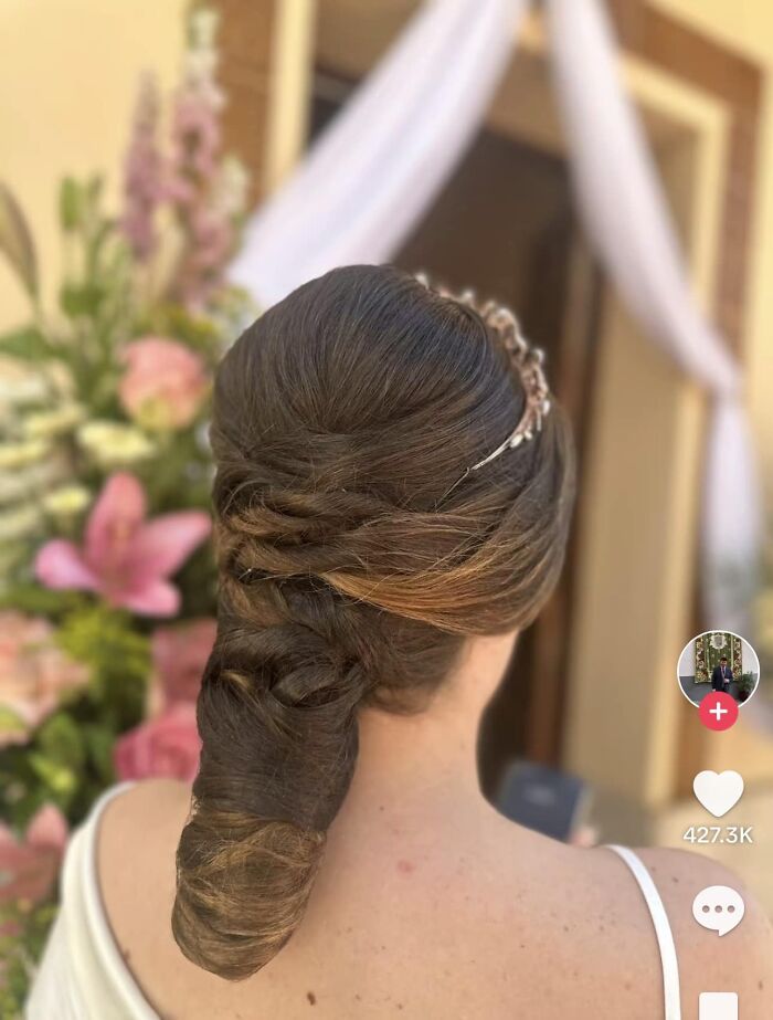 Woman with intricate updo hairstyle featuring twists, standing in a floral backdrop, capturing a hair fail moment.