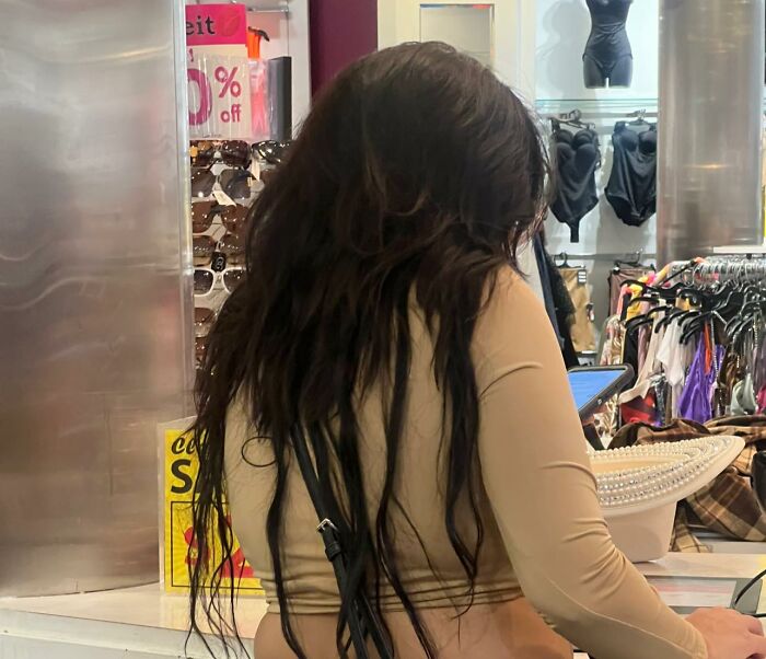 A woman with long, dark hair in a clothing store, possibly experiencing a hair fail.