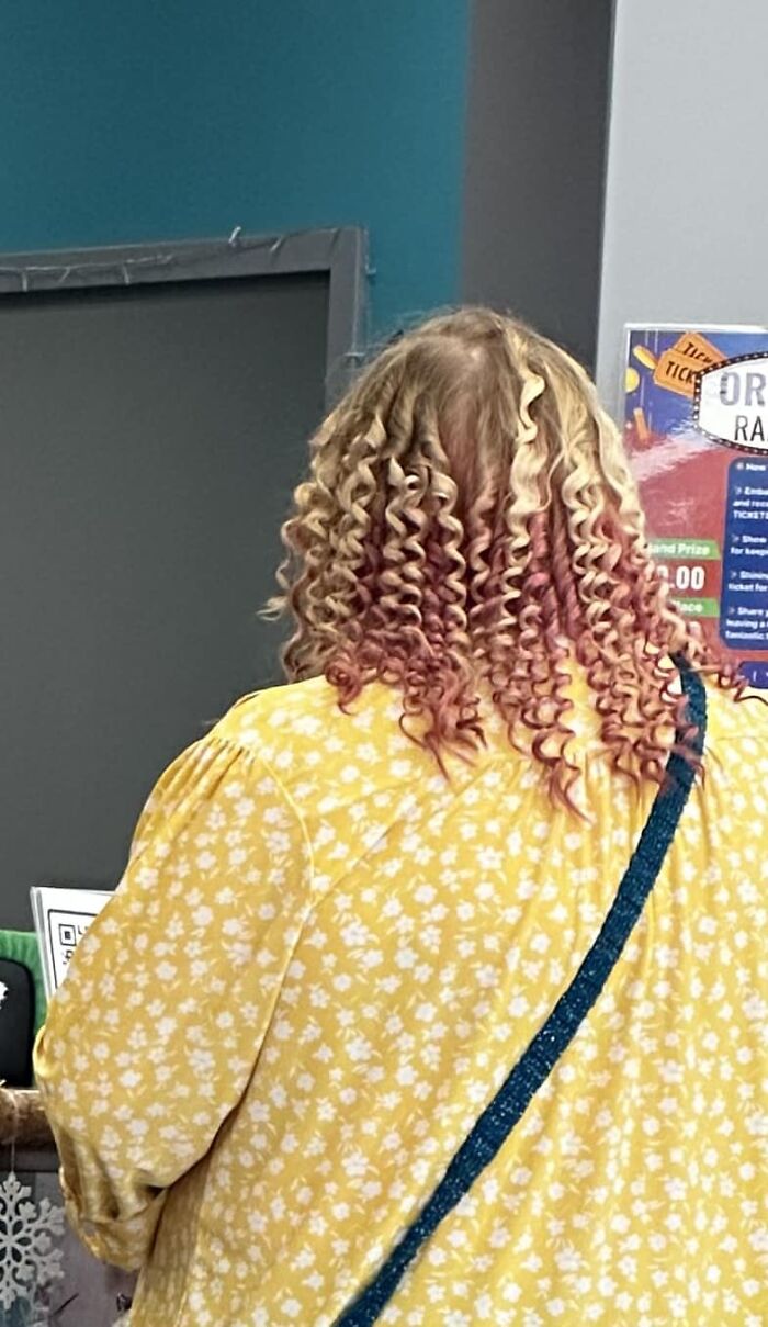 Back view of a person with tight curls dyed in blonde and pink, wearing a yellow floral shirt. Hair fails example.