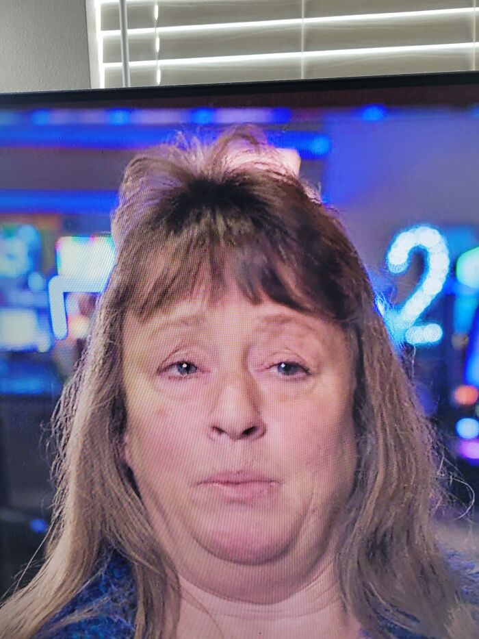 Person with a hair fail, bangs uneven and a tuft sticking up, in a colorful indoor setting.