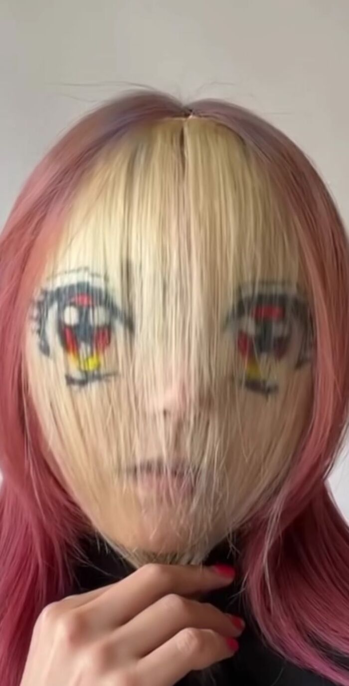 Hair fail with colorful anime-style eyes drawn on blonde bangs, person holding chin.