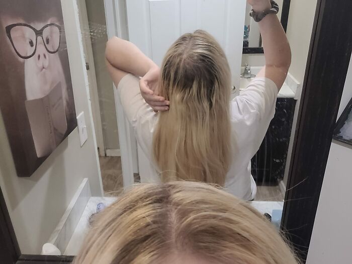 Person showing uneven hair length in the bathroom mirror, illustrating a hair fail.