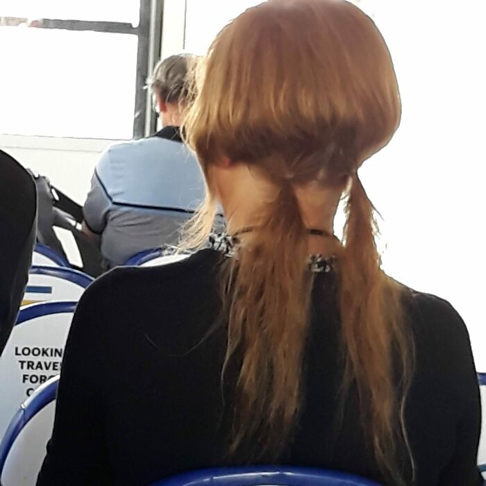 Woman with a hairstyle fail, long hair wrapped awkwardly around her head, sitting in a bus.