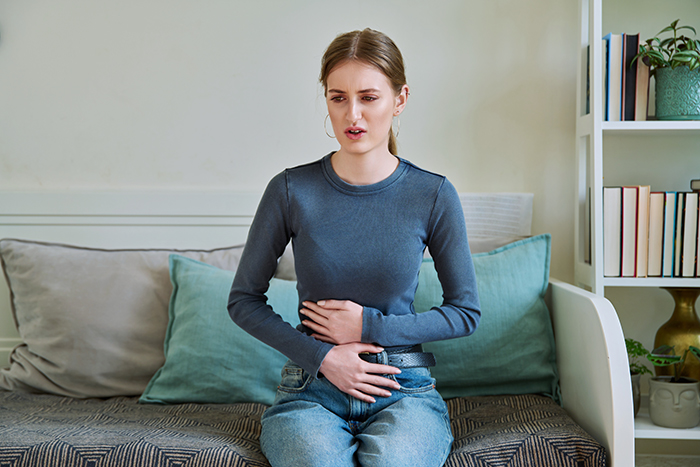 Person experiencing discomfort, holding stomach, possibly due to an allergy, sitting on a couch in a casual setting.