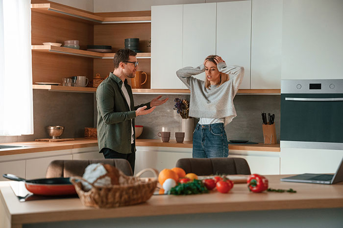 Man and woman in kitchen, discussing weaponized incompetence during an argument.