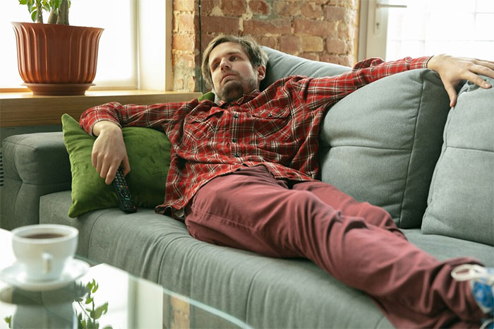 Man in plaid shirt lounging on a couch, representing concept of weaponized incompetence.