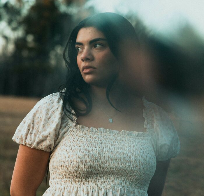 A woman stands outdoors, looking thoughtful, with wedding objection emotions in a serene setting.