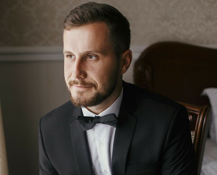 Man in a suit and bow tie, possibly part of wedding objection stories, looking reflective indoors.