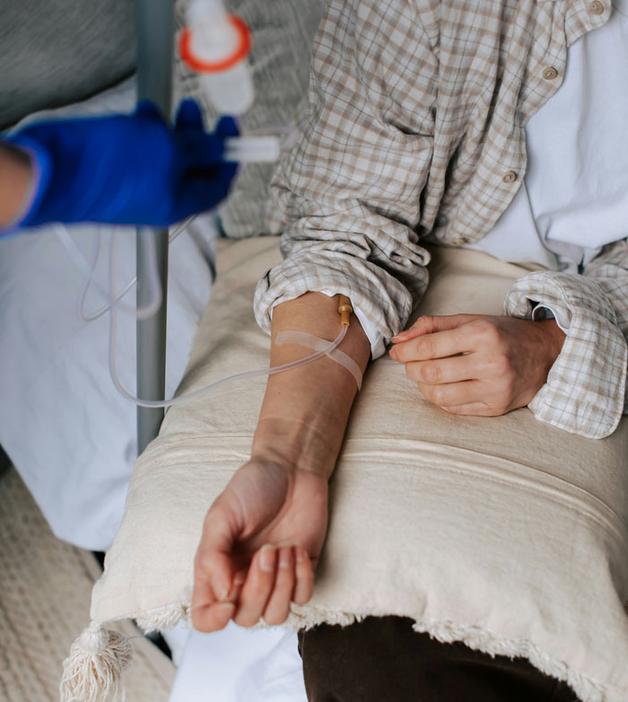 Person receiving chemo treatment, resting on a pillow, wearing a plaid shirt.