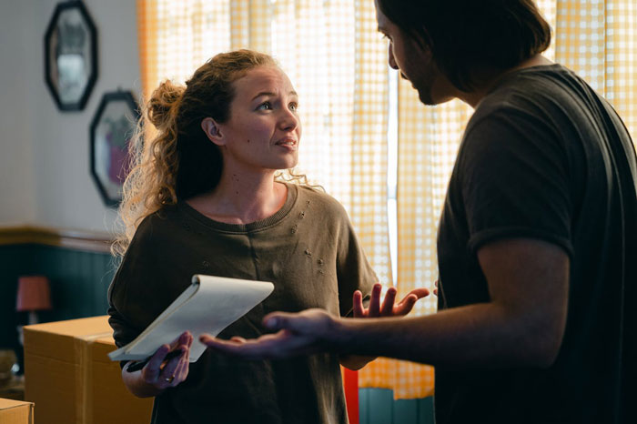 Man and woman discussing wedding issues, holding a notebook, with a tense expression in a home setting.