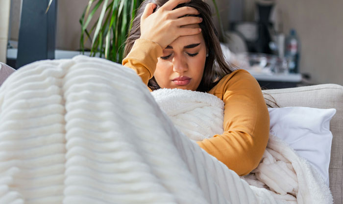 Woman feeling unwell, wrapped in a white blanket, lying on a couch, representing challenges during chemotherapy.