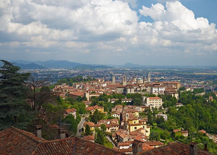 Aerial view of a historic town with red-roofed buildings and lush greenery under a cloudy sky.