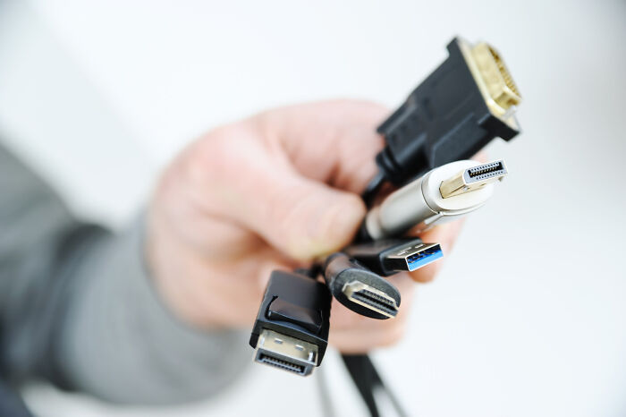 Various cheap cables held in hand, including HDMI and USB, challenging expensive counterparts.