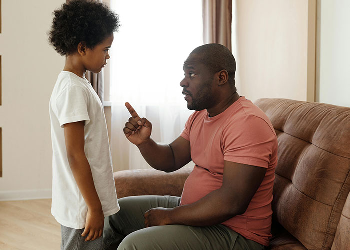 A parent gently explains something to a child, highlighting gentle parenting techniques on a living room couch.