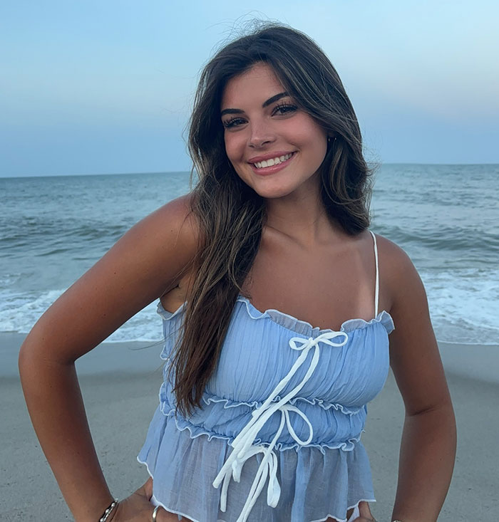 Smiling woman in a blue top at the beach, related to viral romantic note from pilot to plane passenger.