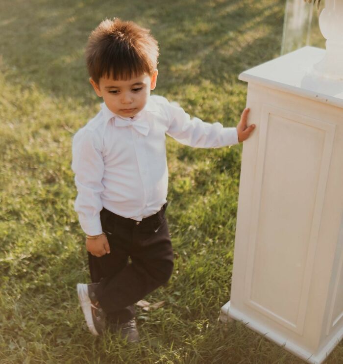 A young boy in formal attire at a wedding venue, positioned by a white pillar.