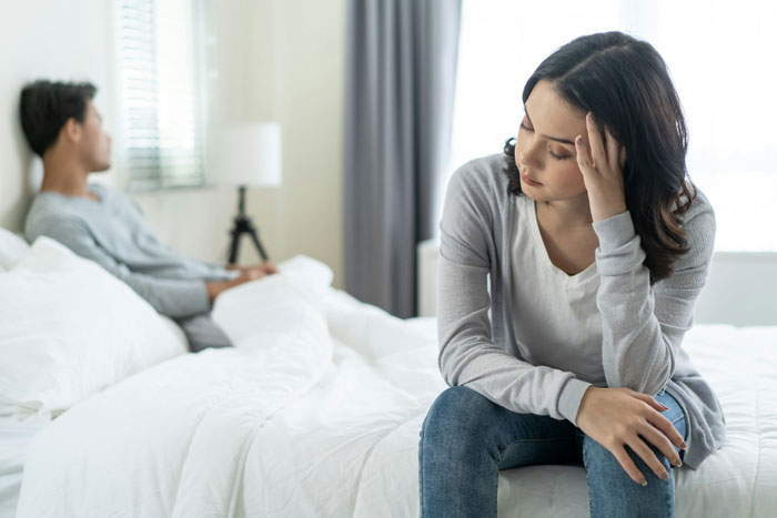 Couple experiencing tension, woman sitting upset on bed, reflecting sterilization decision against partner&rsquo;s wishes.