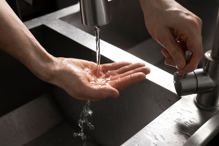 Hands under running water at a kitchen sink, highlighting a cost-effective sink setup.