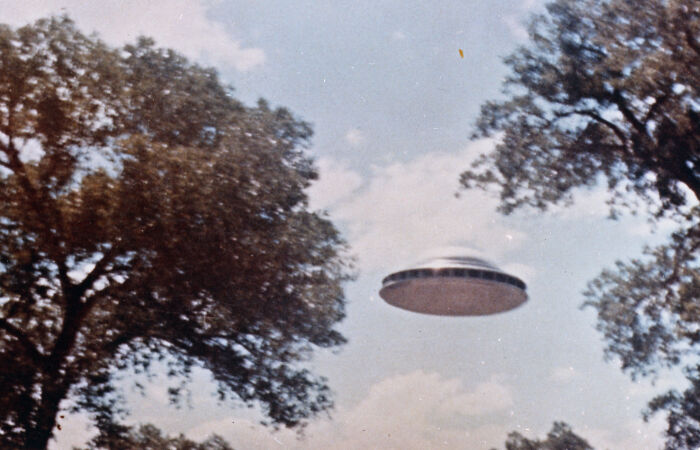 UFO hovering between trees under a cloudy sky, depicting a cool Wikipedia article topic.