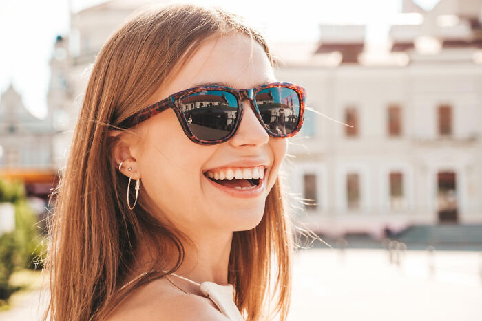 Smiling woman wearing sunglasses outdoors, showcasing a cheap version that beats expensive counterparts.