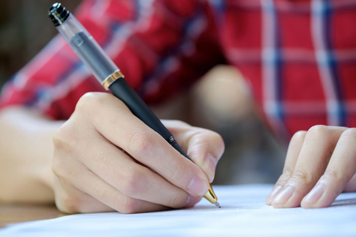 A person in a red plaid shirt writing with a fountain pen on paper, symbolizing inheriting a massive fortune.